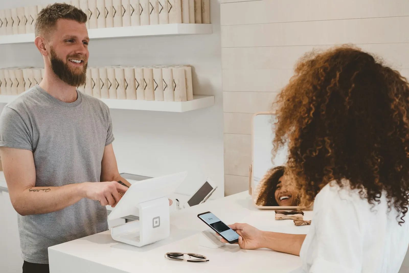 A customer at a shop counter paying by phone while a store assistant helps