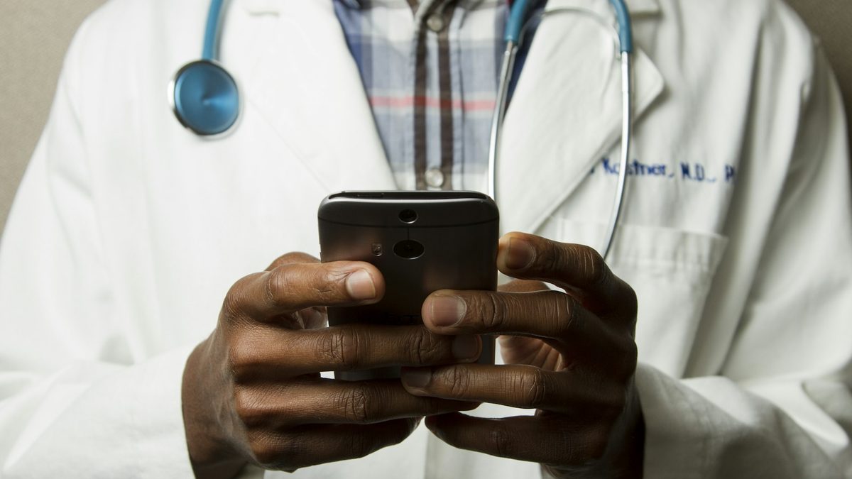 A doctor in a white coat checking a message on a smartphone