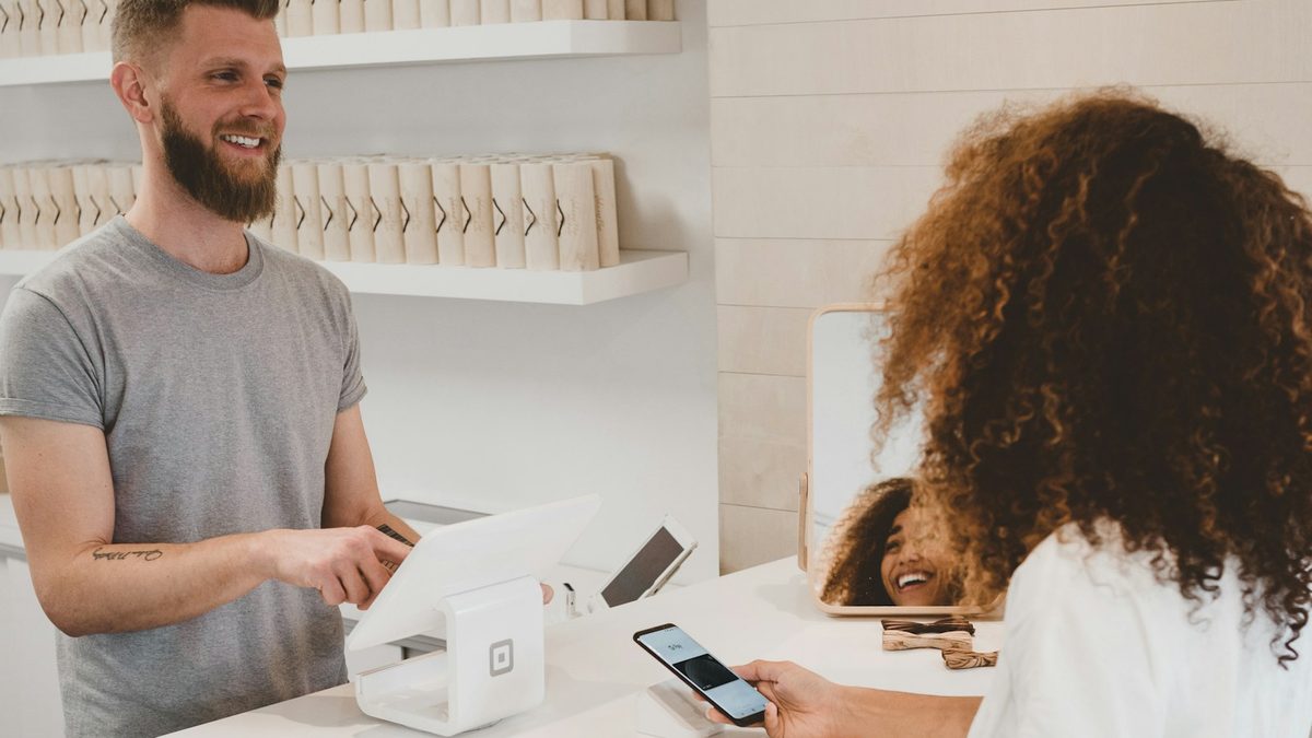 A customer at a shop counter paying by phone while a store assistant helps